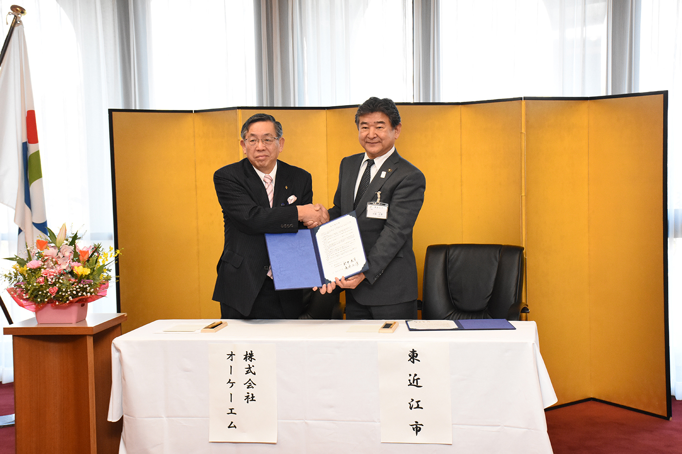 協定書にサインを終え握手する村井代表取締役会長と小椋市長