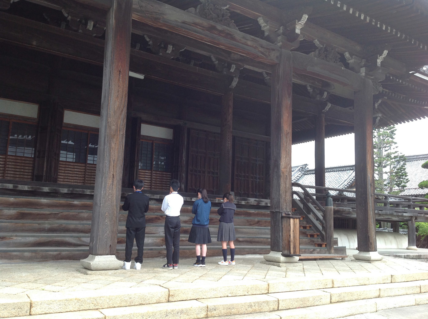 寺の本堂に向かって手を合わせる中学生4人を後ろから撮影した写真