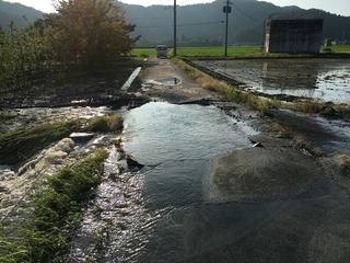 写真：道路が陥没し隣の田から水が流れ込んでいる様子