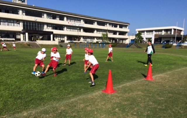 芝生のグラウンドでサッカーを楽しむ小学生
